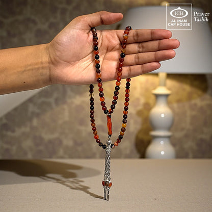 AL INAM CAP HOUSE amber and brown crystal prayer tasbih with silver tassel, held in hand.