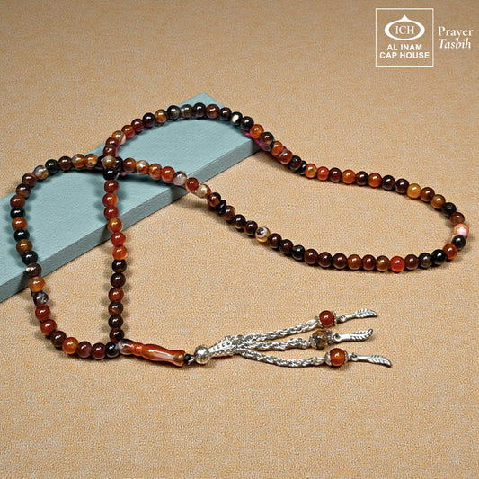 AL INAM CAP HOUSE Belgium Crystal Tasbih with amber, brown, orange, black, and milky beads. Features silver tassel.