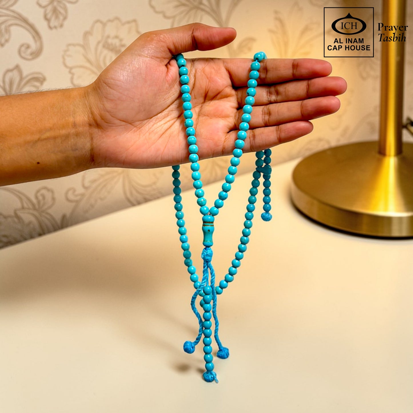 AL INAM CAP HOUSE turquoise Firoza prayer beads tasbih with metallic tassel, held in hand.